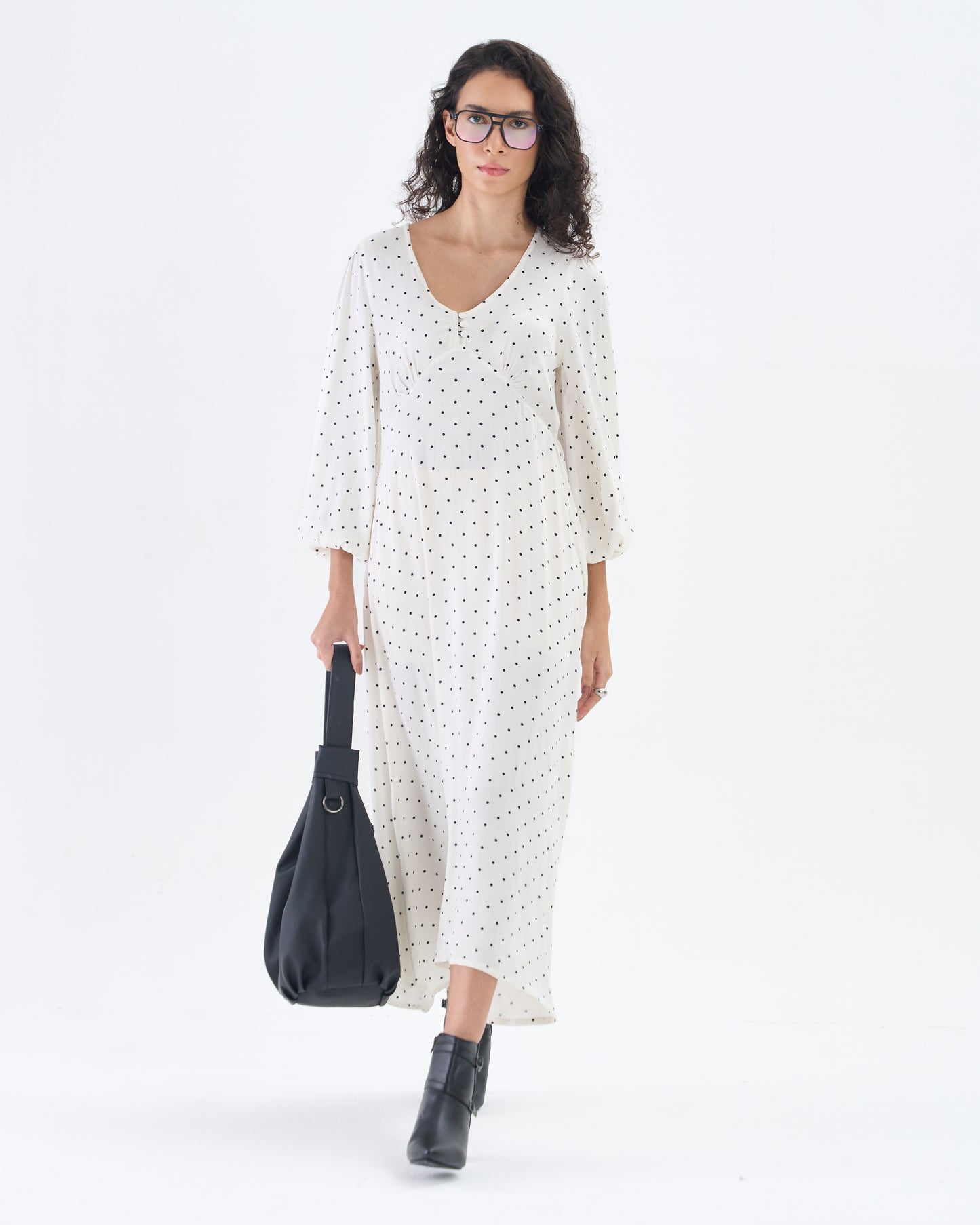 Woman wearing a white dress with black polka dots and holding a black bag on a white background