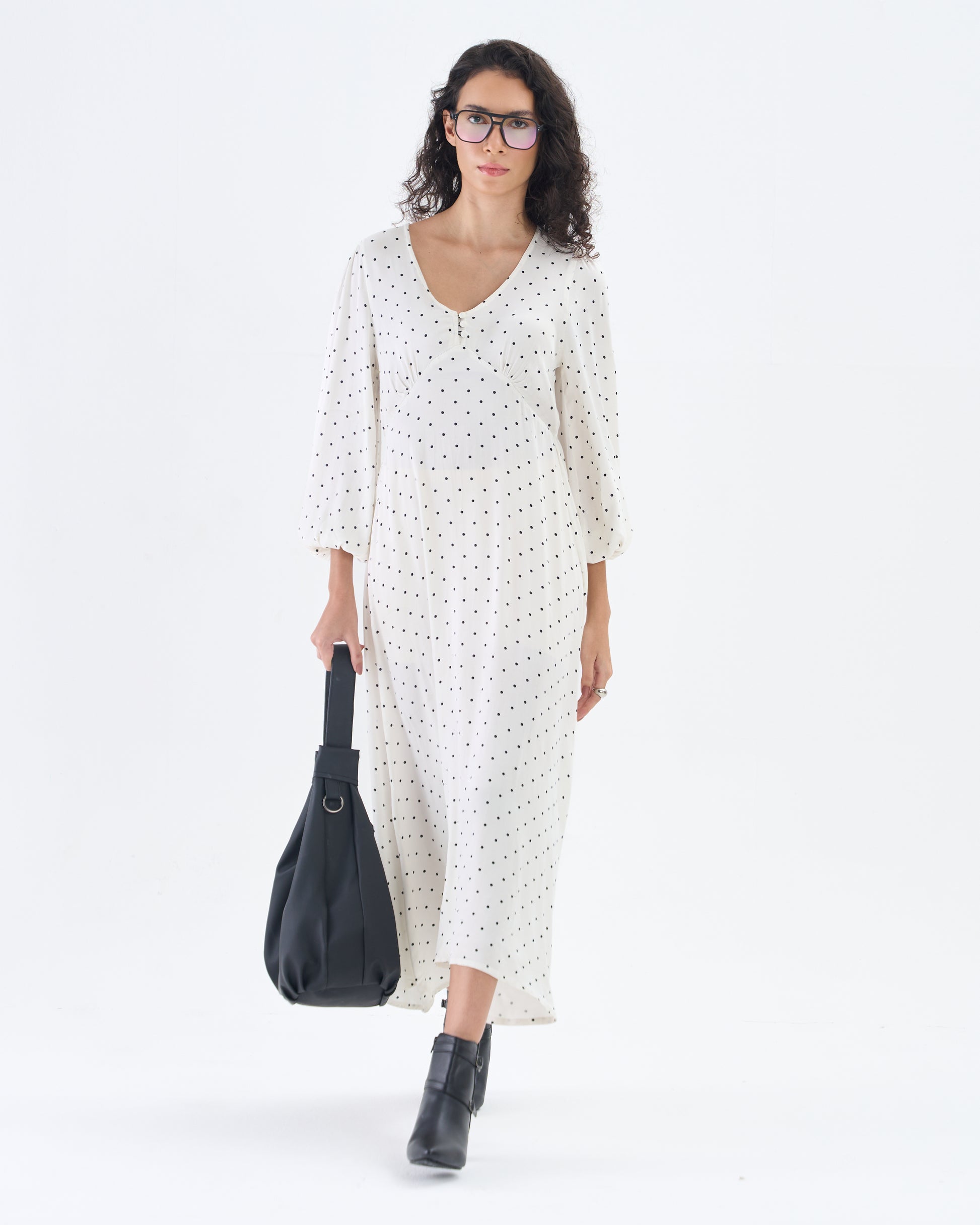 Woman wearing a white dress with black polka dots and holding a black bag on a white background