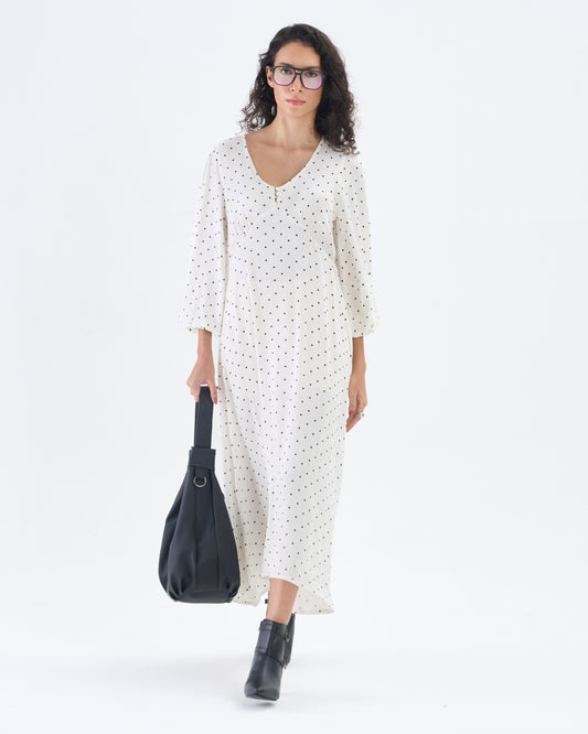 Woman wearing a white dress with black polka dots and holding a black bag on a white background